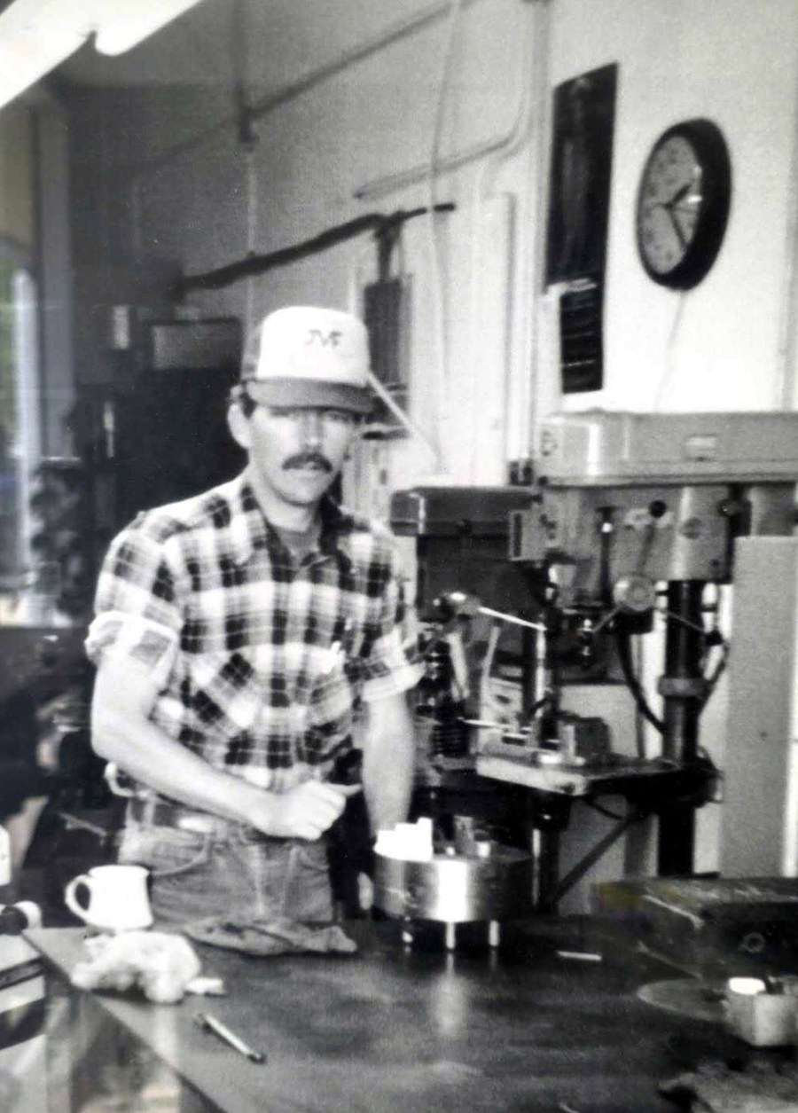 Doug Wilcox at a drill press, a machined part on the bench in front of him